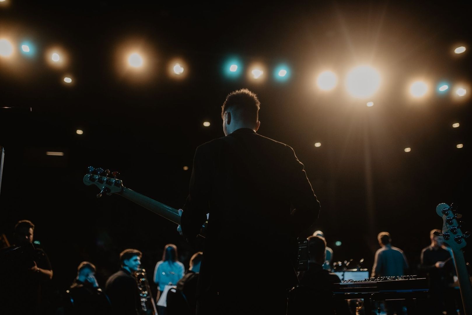 Musician facing bright stage lights with a bass guitar and audience nearby