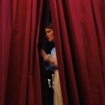 Performer peers through red stage curtains before an entrance