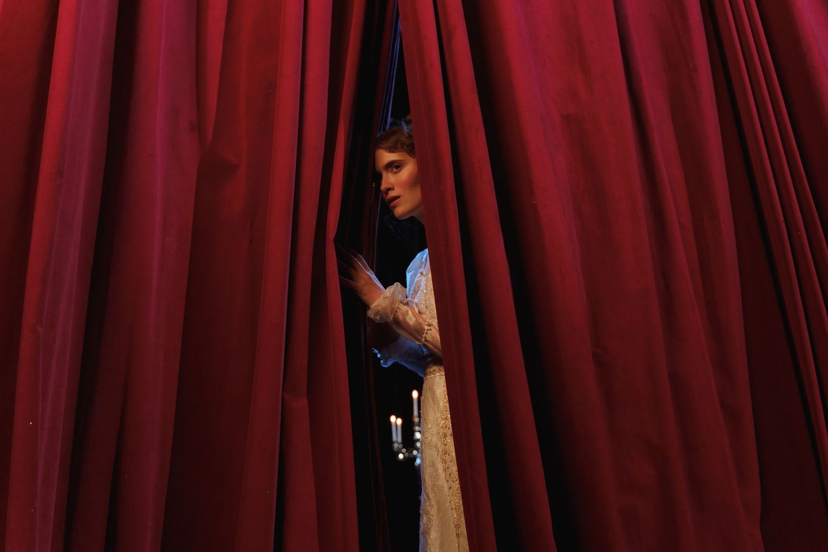 Performer peers through red stage curtains before an entrance